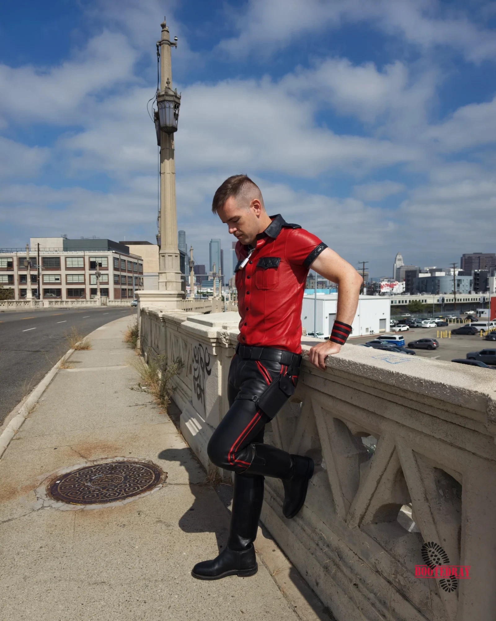 Man in red leather shirt and black pants leaning on concrete railing