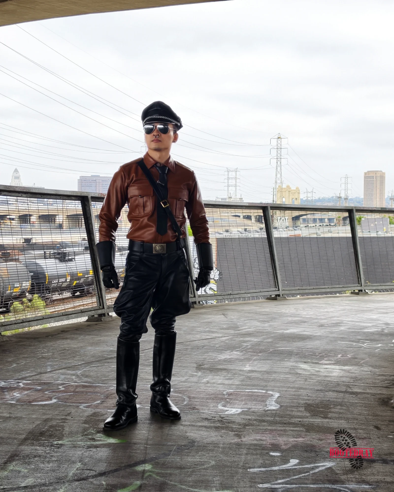 Man in brown leather shirt and black pants with a hat and sunglasses