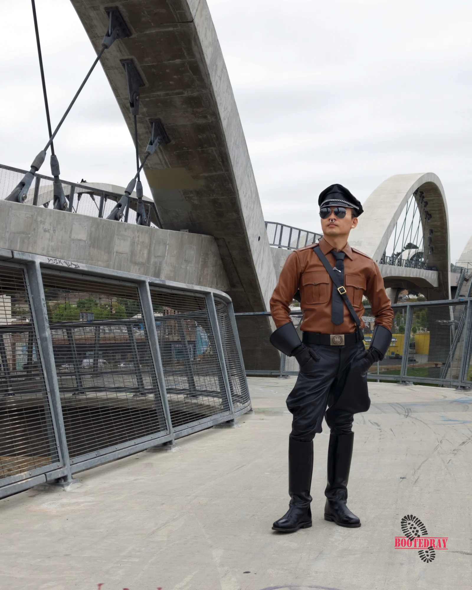 Man in brown leather uniform and black boots standing on a bridge.