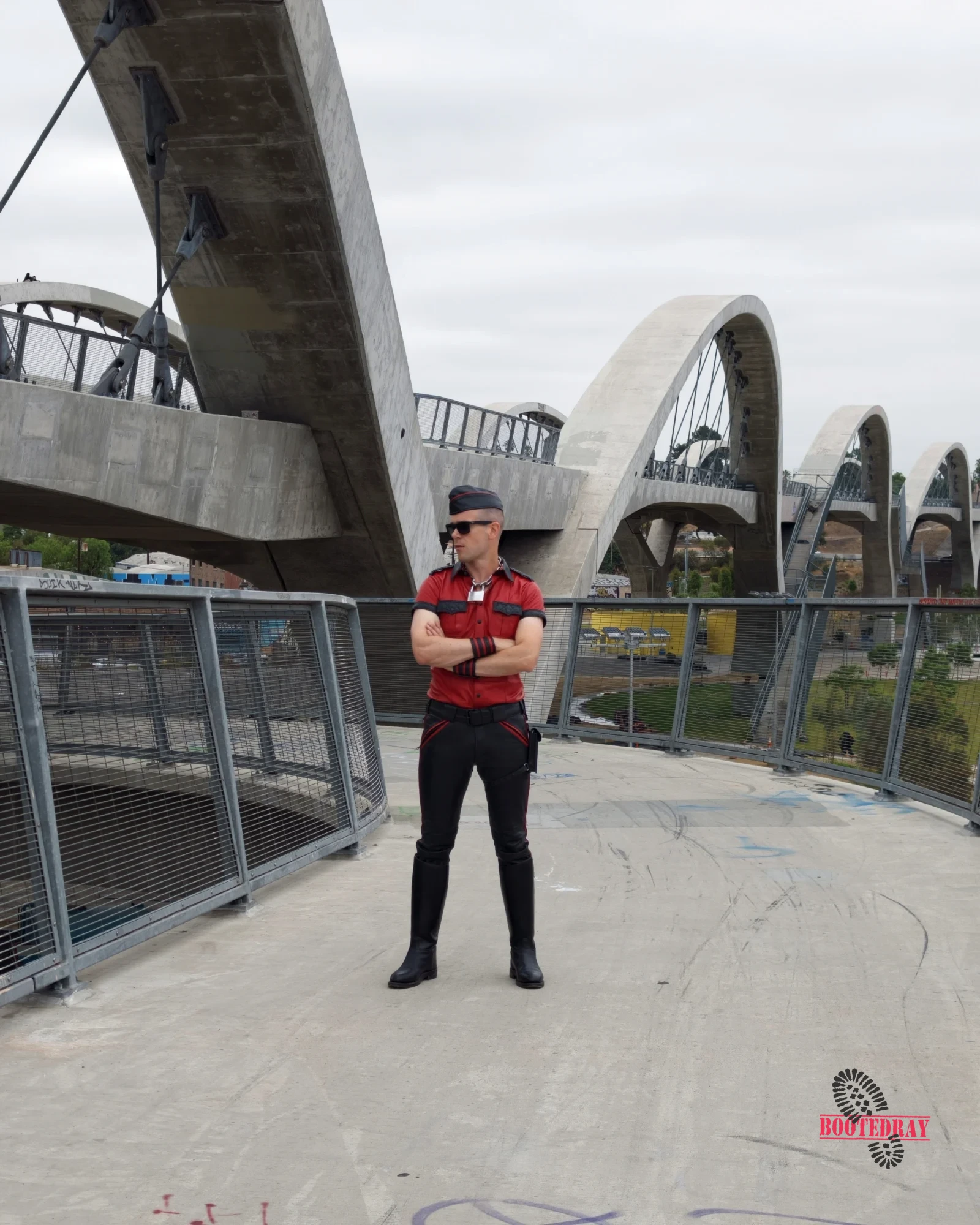 Man in red and black leather uniform and black boots standing on a bridge.