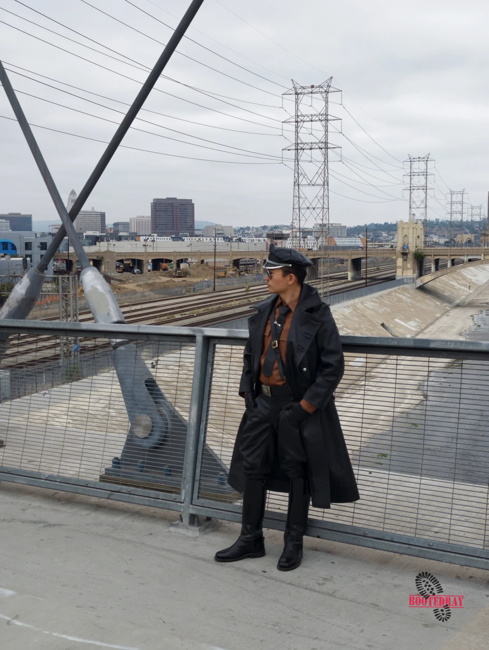 Man in black leather uniform and cap standing on a bridge.