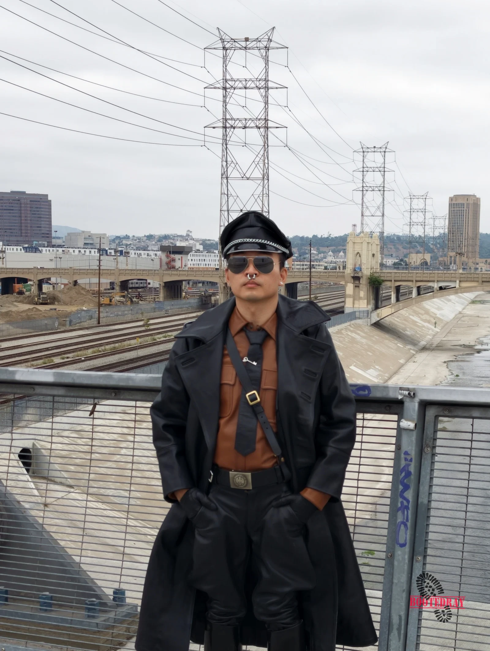 Man in black leather uniform and sunglasses standing on a bridge.