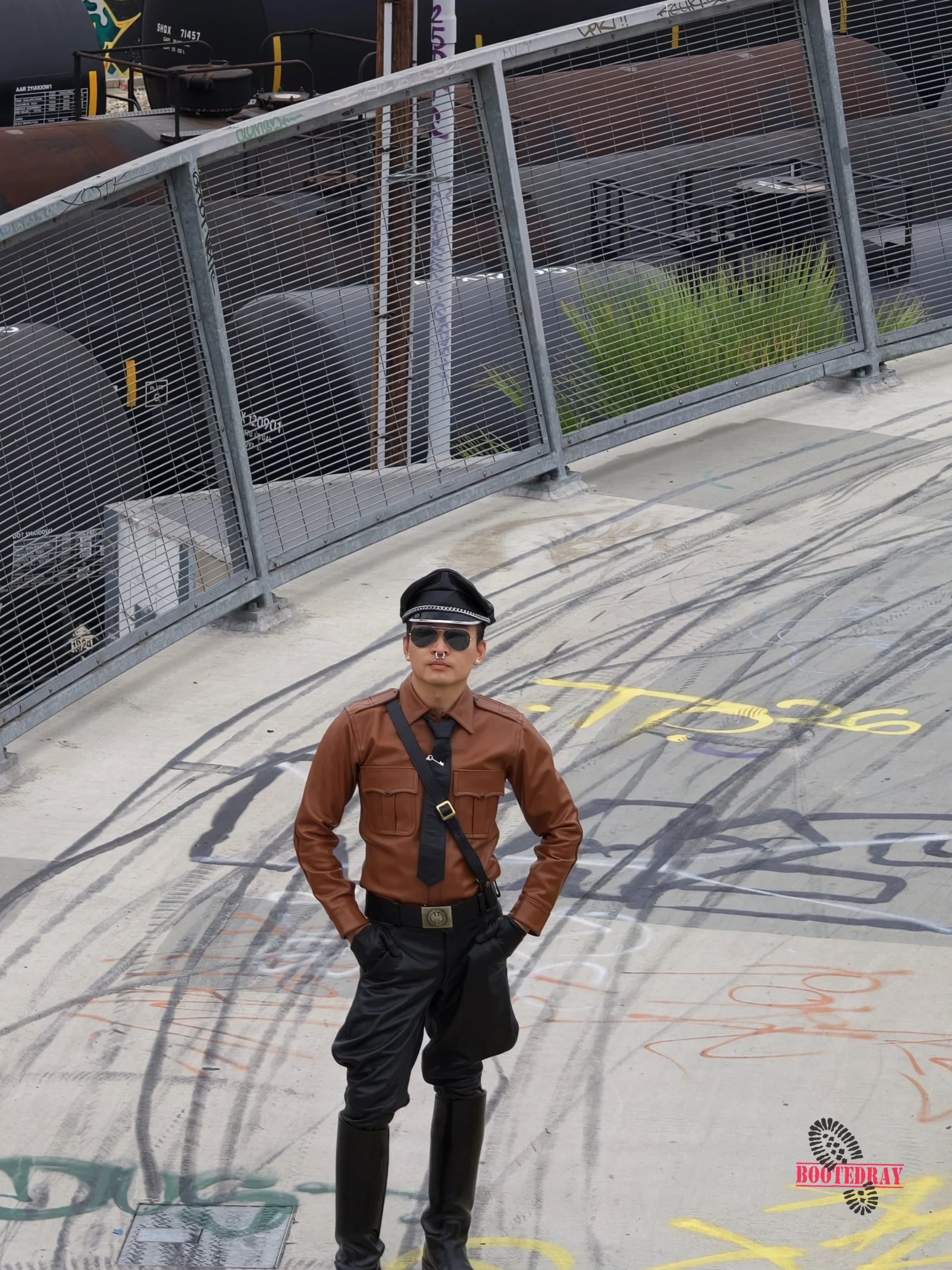 Close up of a man in a brown leather shirt and black hat standing on the bridge.