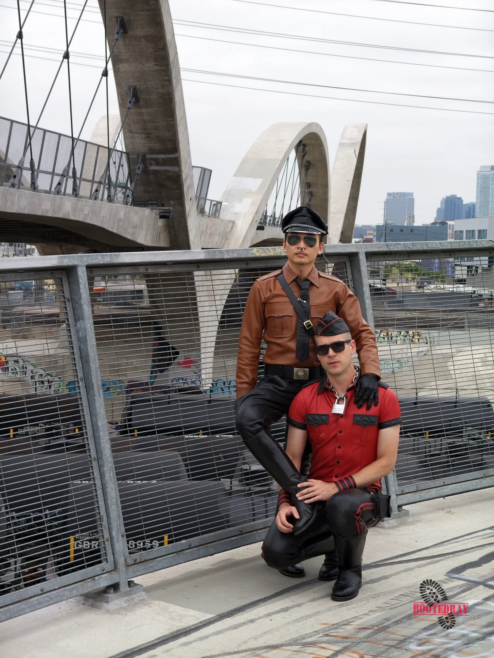 Two men in leather outfits on a bridge with graffiti