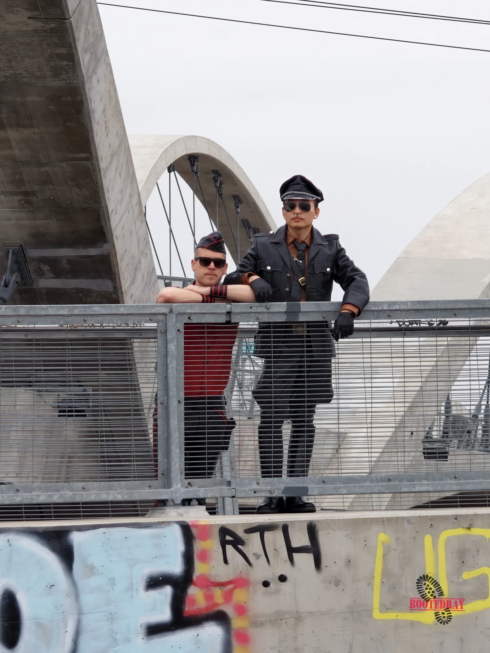 Two men in leather outfits on a bridge with graffiti
