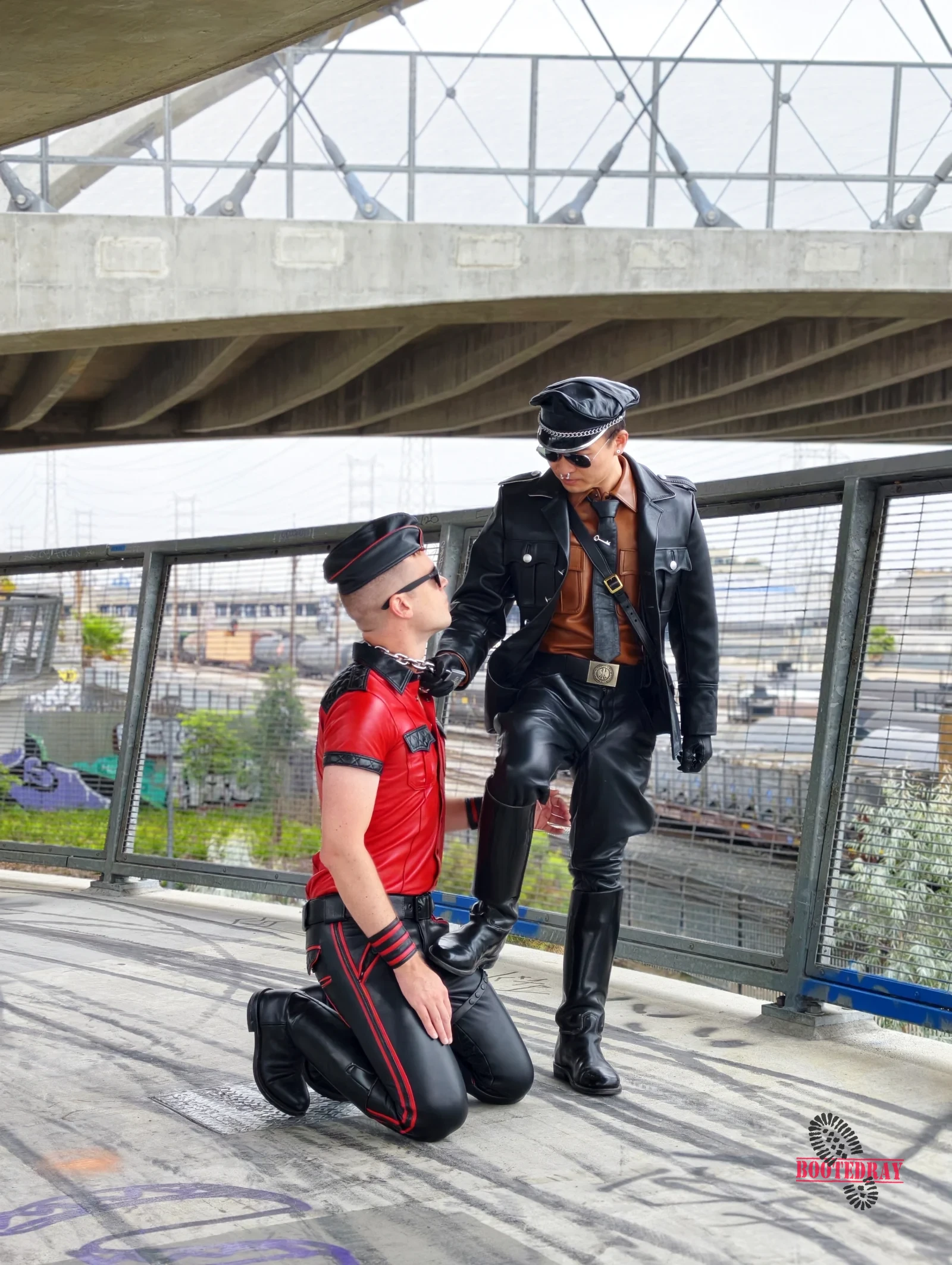 Two men in leather outfits on a bridge with graffiti
